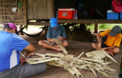 Nathan, Neerav, and Aidan work to connect the palm leaves that will be used to construct kitchen walls. The owner needs 300 panels!